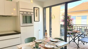 Eine moderne Küche mit Einbauofen und Mikrowelle, ein Essbereich mit Tisch für zwei Personen und Blick auf einen Balkon mit Sitzmöbeln.