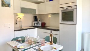 Eine moderne Küche mit weißen Schränken, einem eingebauten Backofen und einer Essecke mit Tisch für zwei Personen.