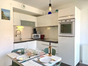 Eine moderne Küche mit weißen Schränken, einem eingebauten Backofen und einer Essecke mit Tisch für zwei Personen.