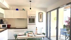 Eine moderne Küche mit weißen Schränken, einem Esstisch für vier Personen und Blick auf den Balkon.