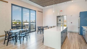 Une cuisine moderne dotée d’un grand îlot central, d’un coin repas avec une longue table et d’une vue dégagée grâce à de grandes fenêtres.