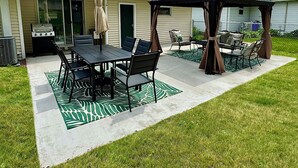 Une terrasse avec une table et des chaises, un barbecue et un kiosque.