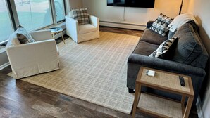 Un salon avec un canapé, un fauteuil et un téléviseur fixé au mur.