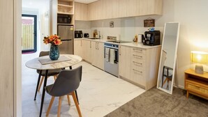 A compact kitchen with a dining area, featuring light wood cabinets, a built-in oven, and a coffee machine.