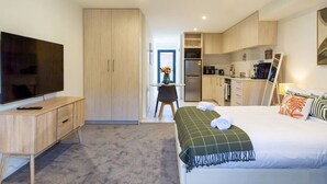 A hotel room with a bed, a TV, a desk, and a kitchenette.
