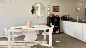 Een moderne keuken met witte kastjes, een ronde spiegel, een boekenkast met modelauto's en een eethoek met een witte tafel en stoelen.