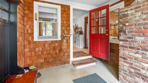 A hallway with a red door, a window with a wooden wall, and a brick wall.