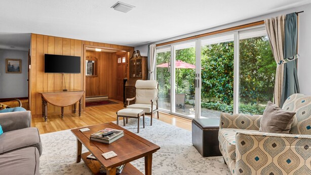 A spacious living room with a wooden floor, a sofa, a coffee table, and a TV mounted on the wall.