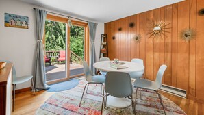 A cozy room with a wooden paneled wall, a round table with chairs, and a large sliding glass door leading to an outdoor deck.