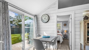 A modern interior with a dining area, a clock, and a view of the outdoors. - Beachside Bliss at Sunset Retreat (West Dennis)