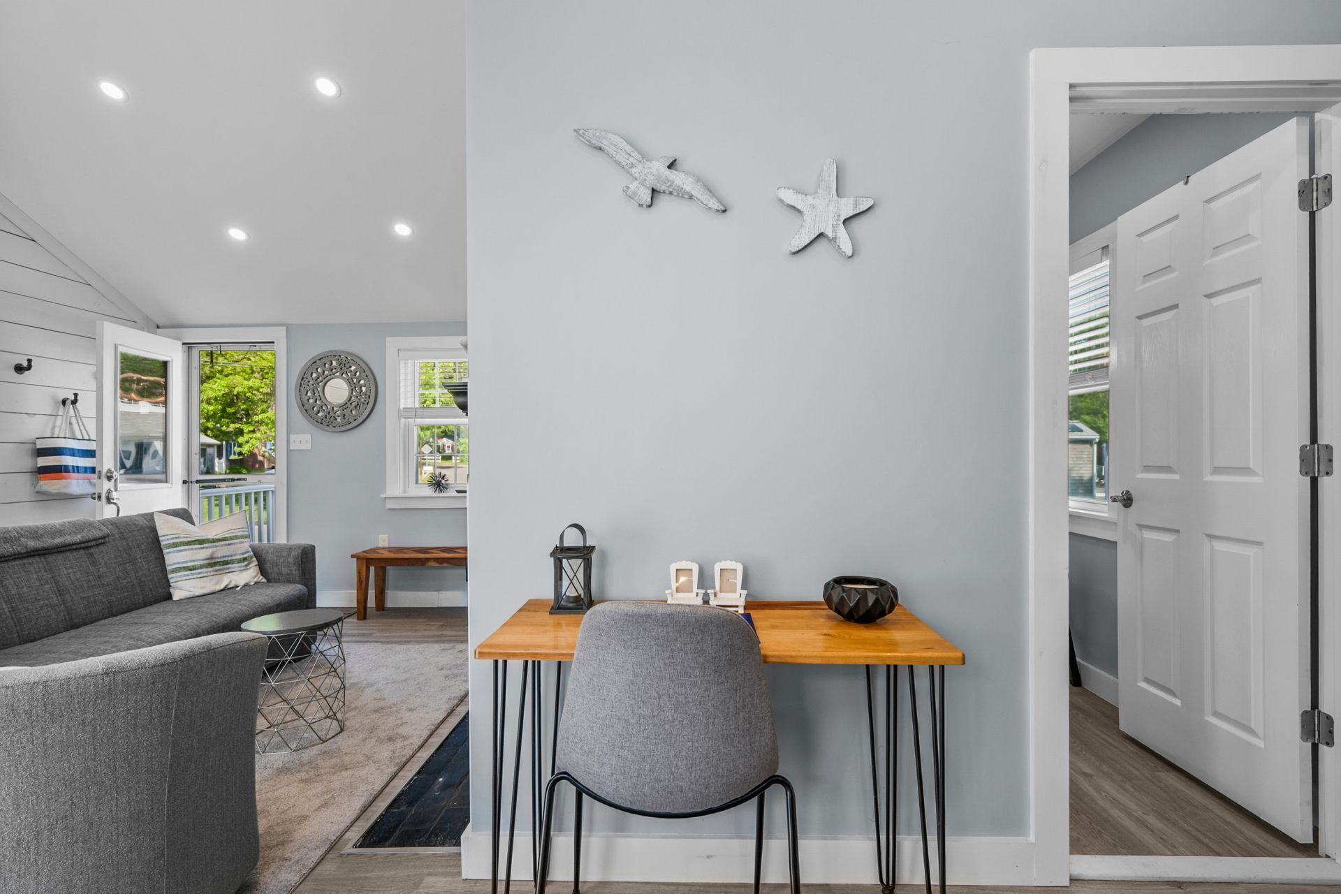 Ein modernes Wohnzimmer mit einem grauen Sofa, einem Holzesstisch und einem grauen Sessel. An der Wand hängt eine Dekoration in Form eines Seesterns und eine Wanduhr.