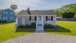 A two-story house with a front porch, a chimney, and a small front yard with a gravel driveway. - Beachside Bliss at Sunset Retreat (West Dennis)