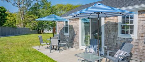 A patio with outdoor furniture and umbrellas, a glass door, and a wooden fence in the background.
