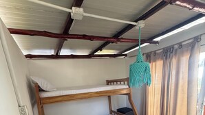 Una cama litera con estructura de madera, una lámpara colgante, un tapete a rayas verdes y una planta.