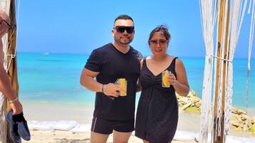 Une enseigne en bois sur laquelle on peut lire « Shekina Club House », placée sur fond de plage.