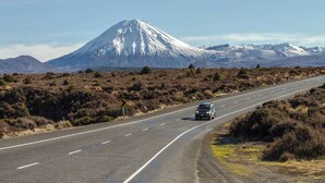 A road with a vehicle, surrounded by mountainous terrain and sparse vegetation.