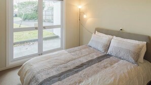 A bedroom with a large window, a bed with a grey headboard, and a floor lamp.