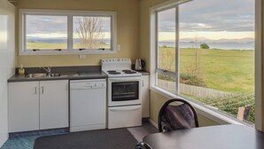 A kitchen with a view of a grassy field and mountains, a stove, a sink, and a clock on the wall.