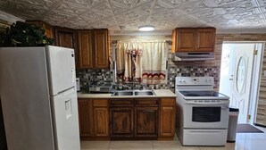A kitchen with a patterned ceiling, wooden cabinets, a refrigerator, a stove, and a sink.