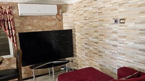 A living room with a TV, red sofa, stone wall, and patterned ceiling.