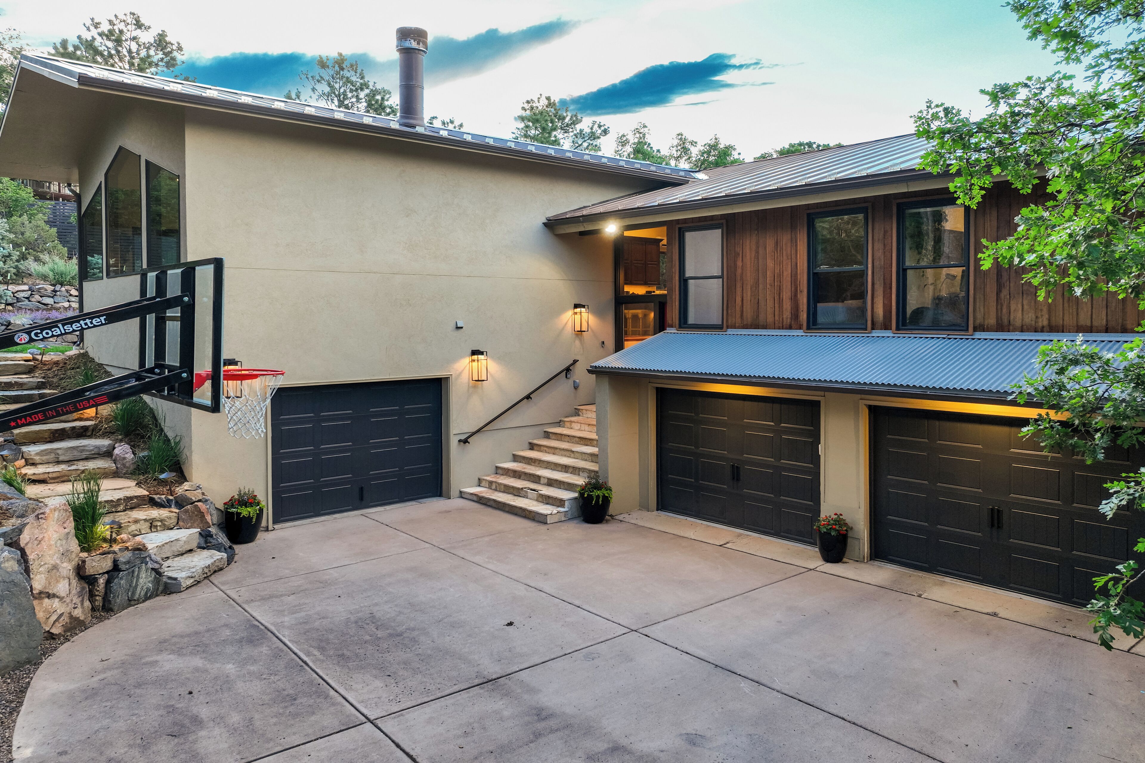 A modern house with a concrete driveway, two garage doors, a staircase, and a basketball hoop.