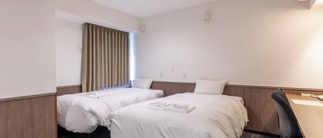 Habitación de hotel con dos camas individuales, un escritorio con silla, ventana con cortinas y aire acondicionado.