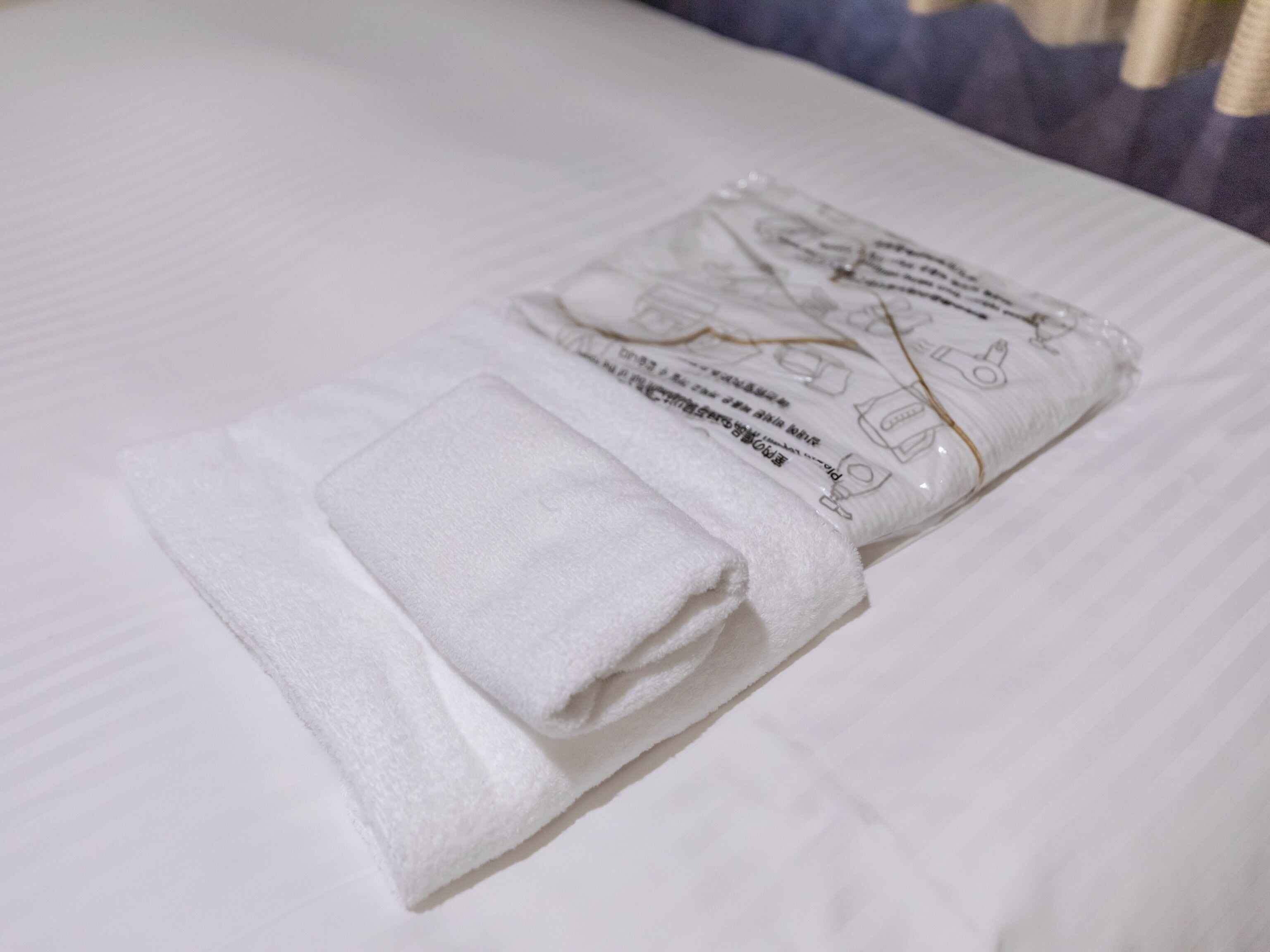 Toalha branca dobrada sobre uma cama com lençol branco.