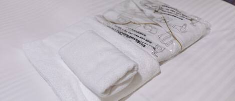 Toalha branca dobrada sobre uma cama com lençol branco.