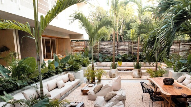A spacious outdoor area with a wooden table, beige sofas, and potted plants.
