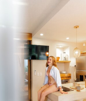 Une femme est assise sur un comptoir de cuisine, dans une cuisine moderne équipée d’un réfrigérateur, d’une cuisinière et d’un luminaire suspendu.