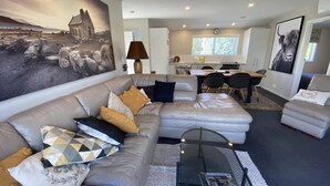 A modern living room with a sofa, a coffee table, and a dining area with chairs. - Southern Comfort Twizel Escape (Twizel)