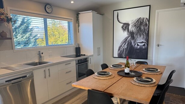 A modern kitchen with a dishwasher, oven, and a dining area with a wooden table set for four. - Southern Comfort Twizel Escape (Twizel)