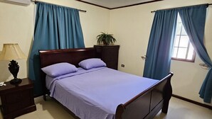 Un dormitorio con una cama de madera, una mesita de noche, una lámpara, una planta en maceta y cortinas azules.