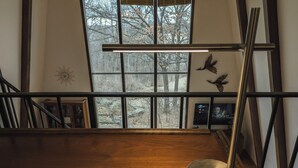 Ein Zimmer mit großem Fenster, Holzboden, einer Stehlampe und einer an der Wand befestigten Uhr.
