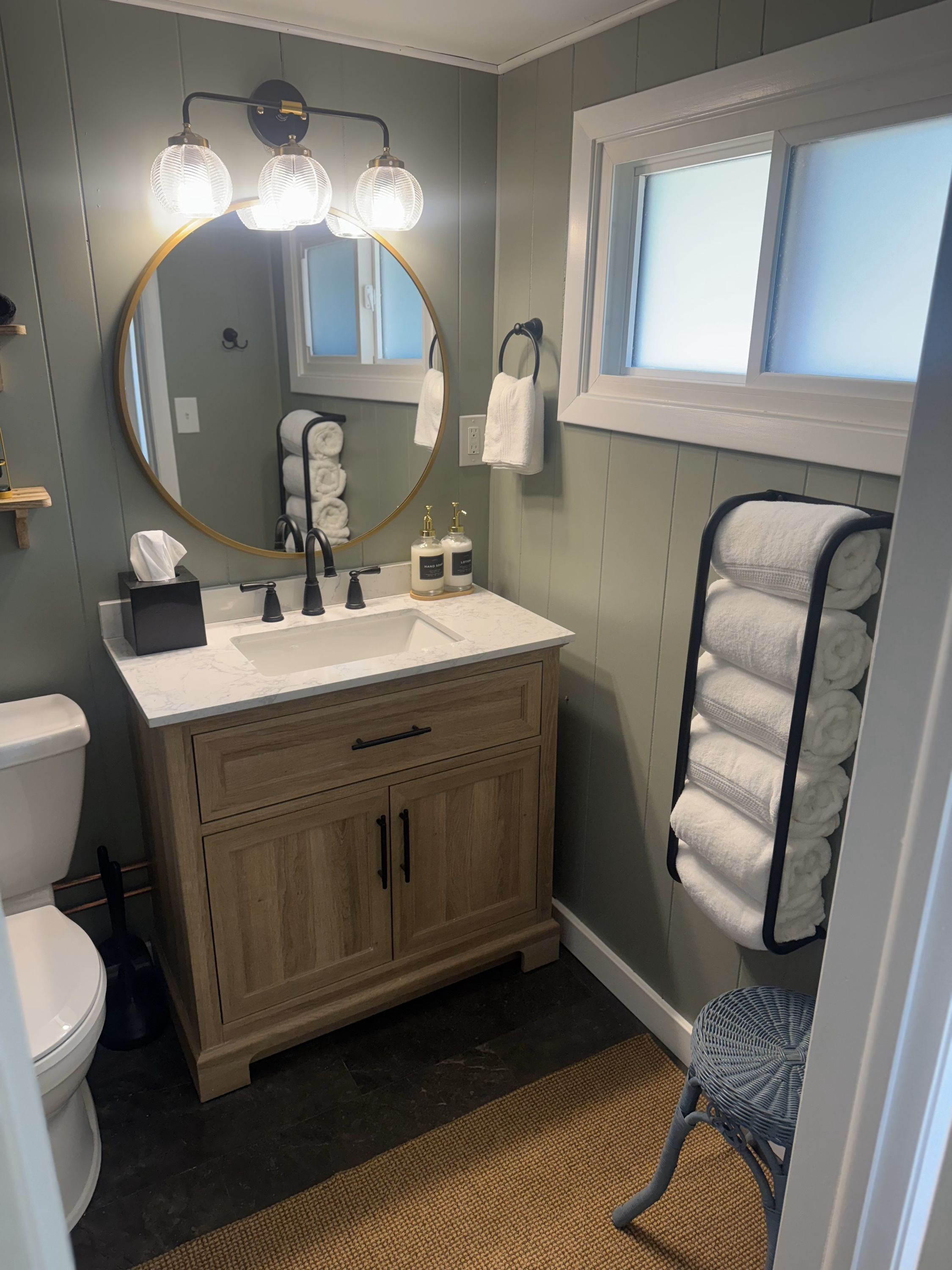 Une salle de bain avec un miroir rond, un lavabo doté d’un robinet doré et un porte-serviettes où sont soigneusement pliées les serviettes.