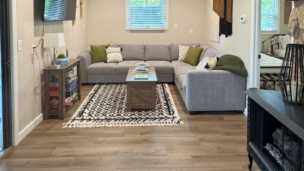 A spacious living room with a wooden ceiling, a grey sofa set, a patterned rug, and a television mounted on the wall. - Waubee Lake Remodeled Cozy Cottage on ATV Trails (Lakewood)