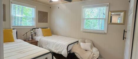 A compact bedroom with two beds, a ceiling fan, and two windows with blinds.