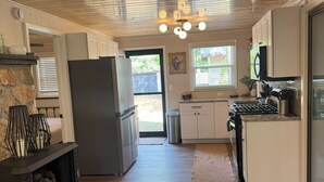 A kitchen with wooden floors, white cabinets, a stone fireplace, and a modern stove. - Waubee Lake Remodeled Cozy Cottage on ATV Trails (Lakewood)