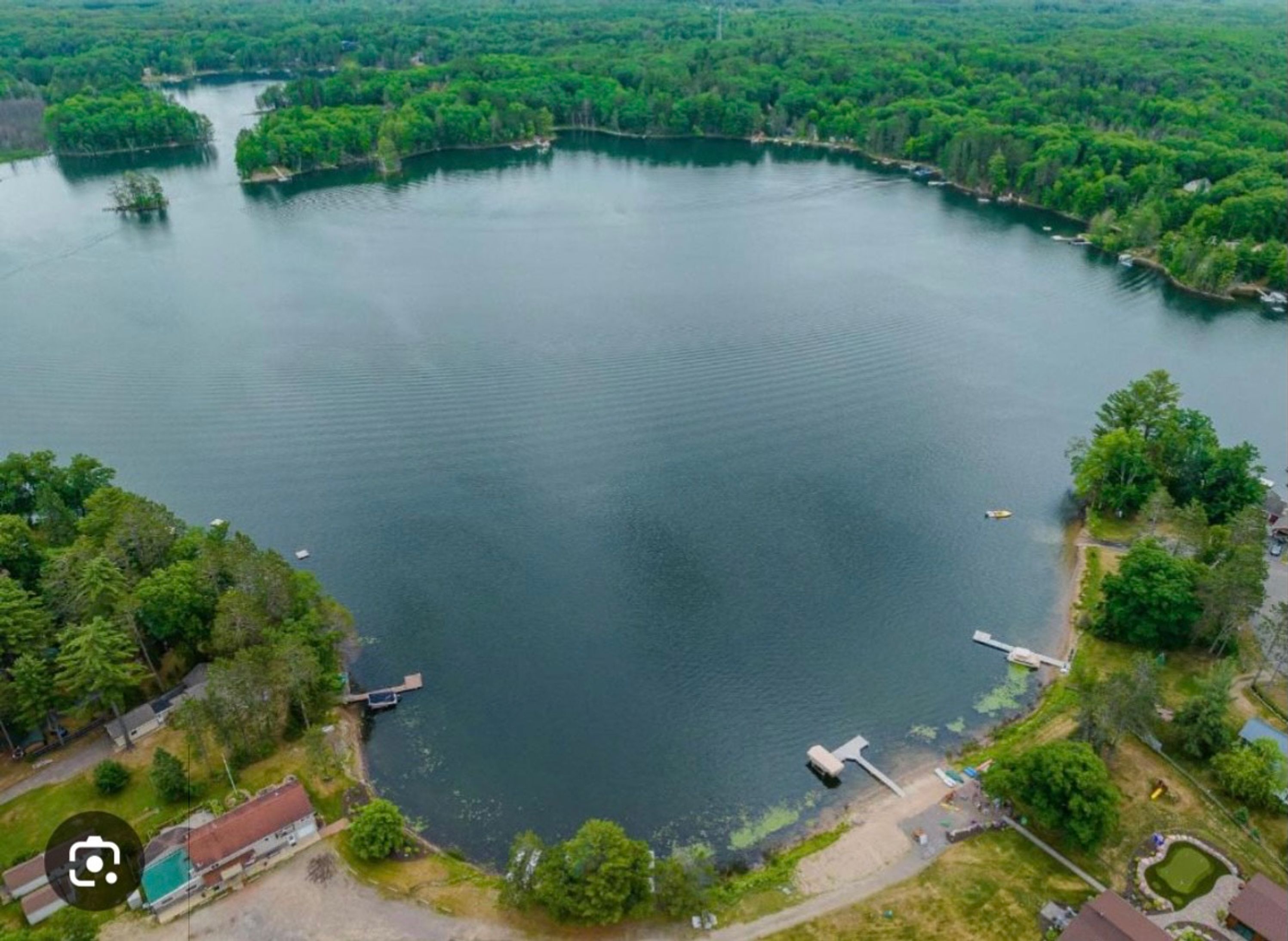 Vue aérienne d’un lac entouré d’une forêt dense et de zones résidentielles.