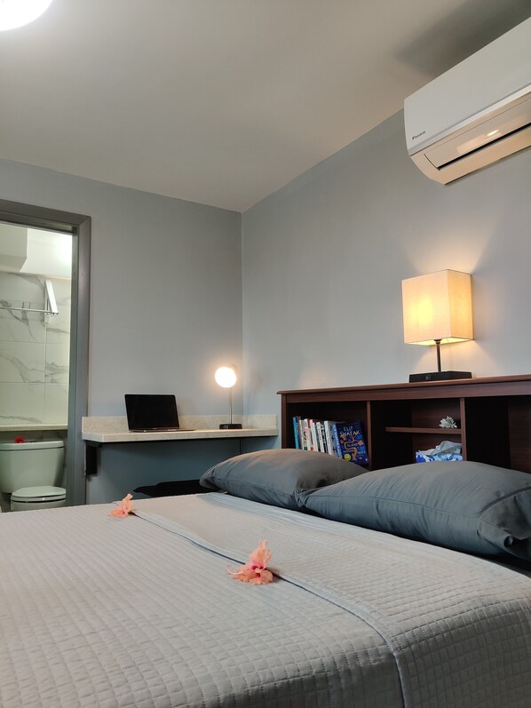 Habitación de hotel con una cama, una mesita de noche con lámpara, una computadora portátil y una estantería.