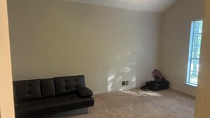 Une pièce avec un canapé en cuir noir, un ventilateur de plafond et une fenêtre avec des stores.