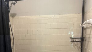 Une salle de bain avec une baignoire, une douche et des murs carrelés. On peut voir trois paniers en métal accrochés au mur, ainsi qu’un distributeur de serviettes.