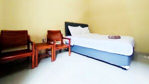 A small, simple room with a bed, two wooden chairs, and a nightstand. - Omah Sewu 68 By Reccoma (Surabaya)