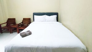 A single bed with white bedding, a dark headboard, and two wooden chairs against a plain wall. - Omah Sewu 68 By Reccoma (Surabaya)