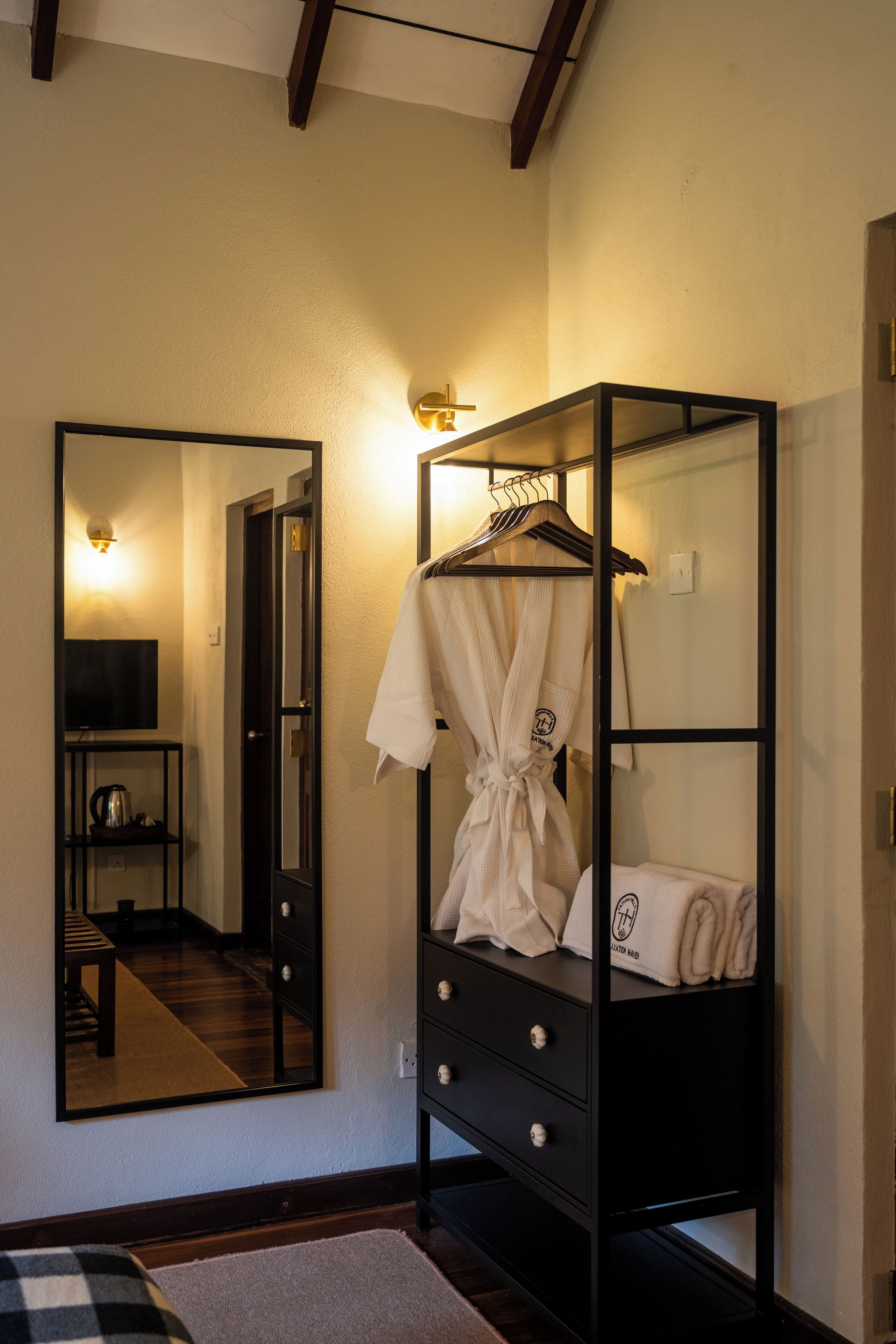 Una habitación de hotel con un espejo grande, un armario negro, una bata y un televisor.