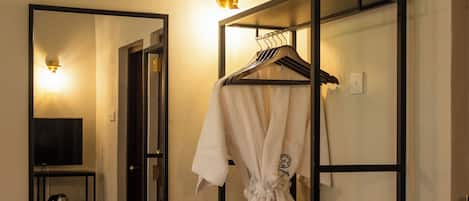 A hotel room with a large mirror, a black wardrobe, a robe, and a television.
