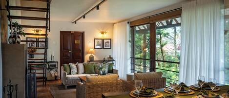 A cozy living room with a sofa, a dining table set for a meal, and a large window with curtains.