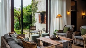 A cozy outdoor seating area with wicker furniture, a wooden table, and a view of a garden and building in the background. - Tathya Hills - Luxe Garden Retreat (Nuwara Eliya)