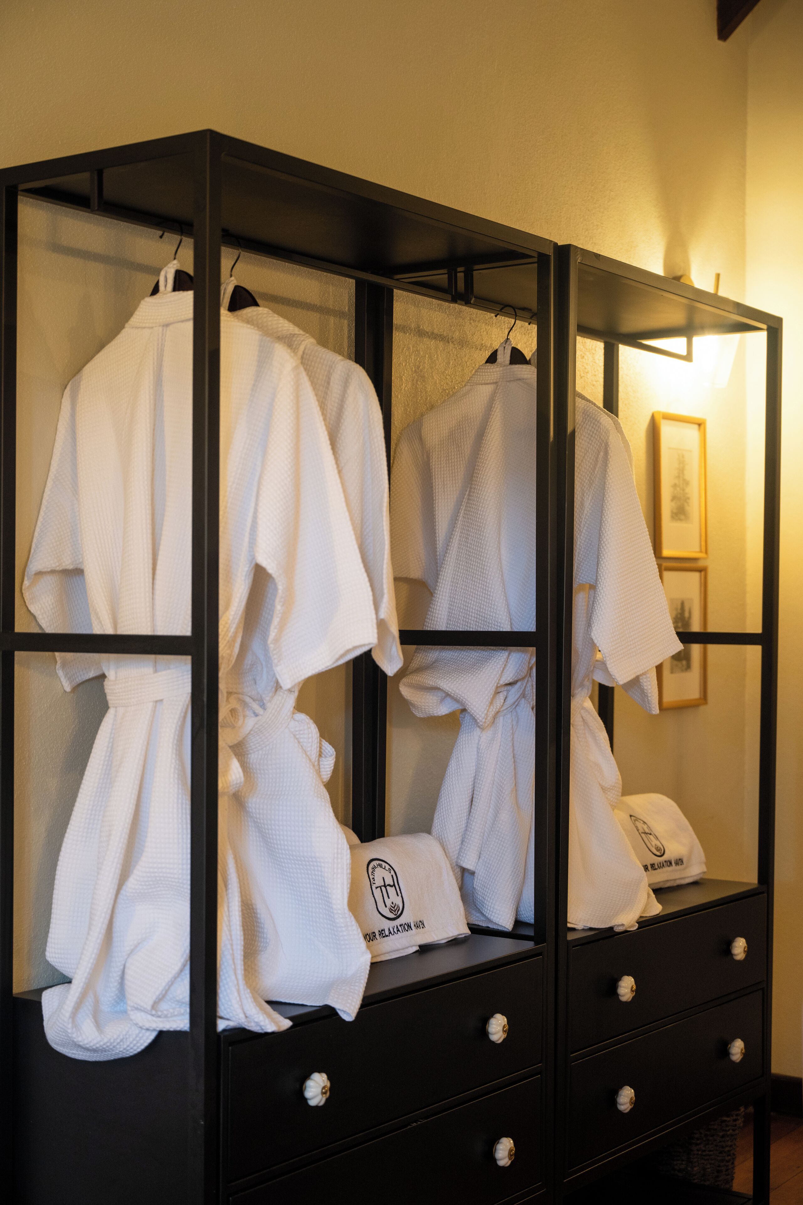 A black wardrobe with multiple drawers and a mirrored section, containing white robes and towels.