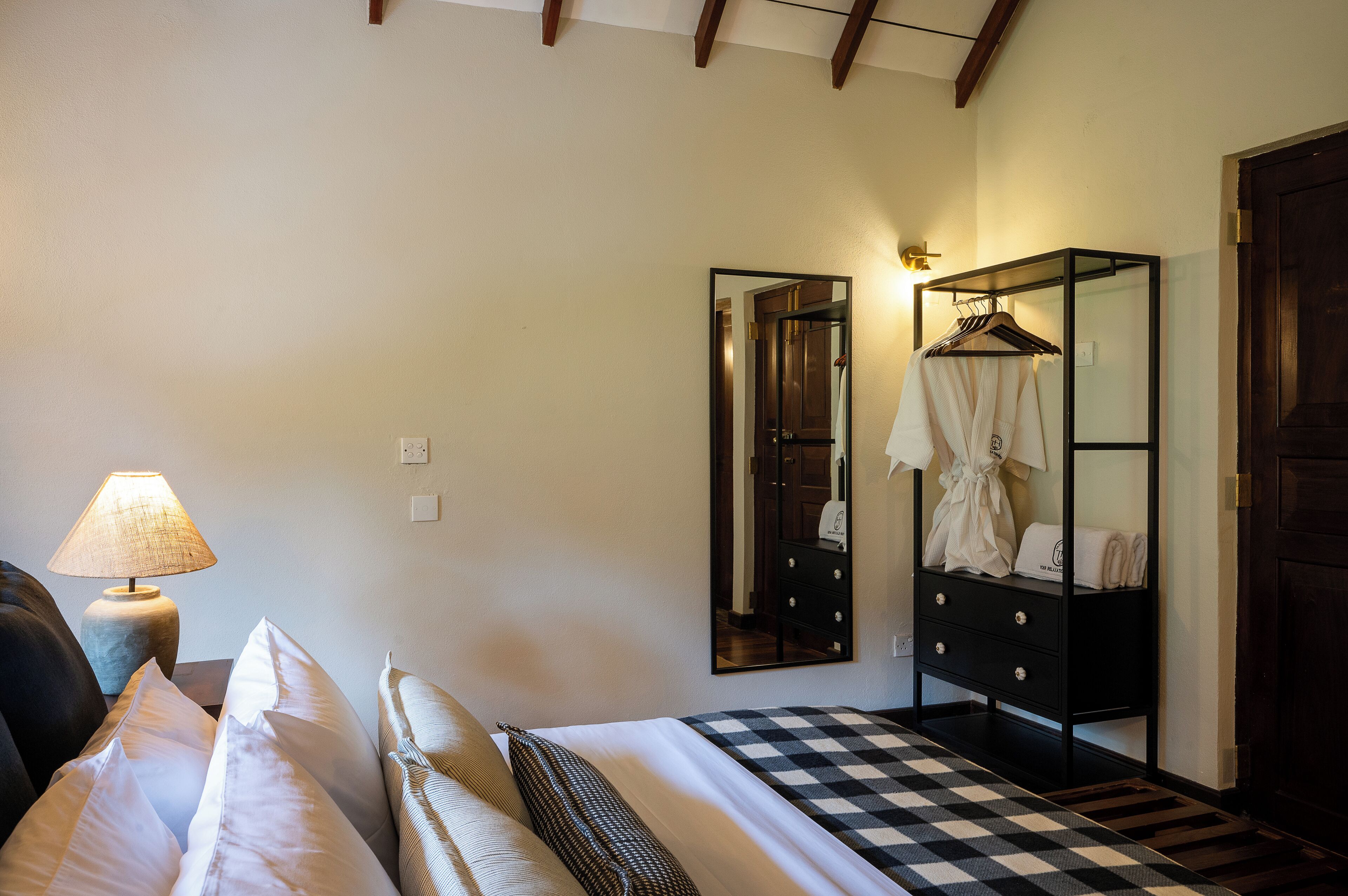 A bedroom with a bed, pillows, a lamp, a dresser, and a mirror.